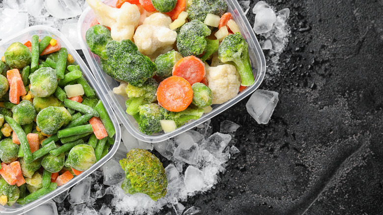 Two plastic containers filled with frozen vegetables on ice