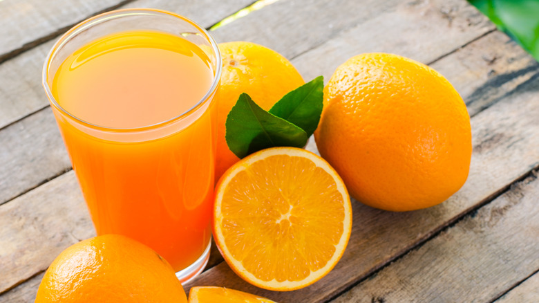 A glass of orange juice with several oranges, one of which is cut in half