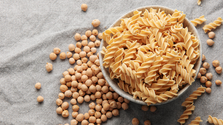 A bowl full of chickpea pasta with chickpea beans spilled out beside it