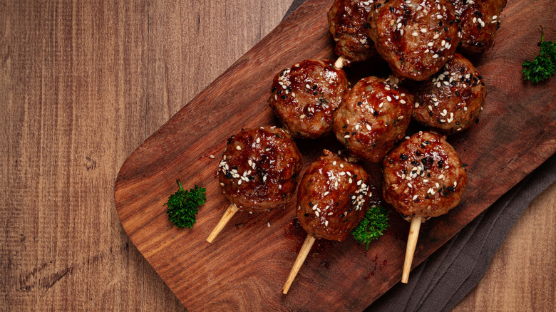 meatball skewers covered with sesame seeds on a wooden cutting board