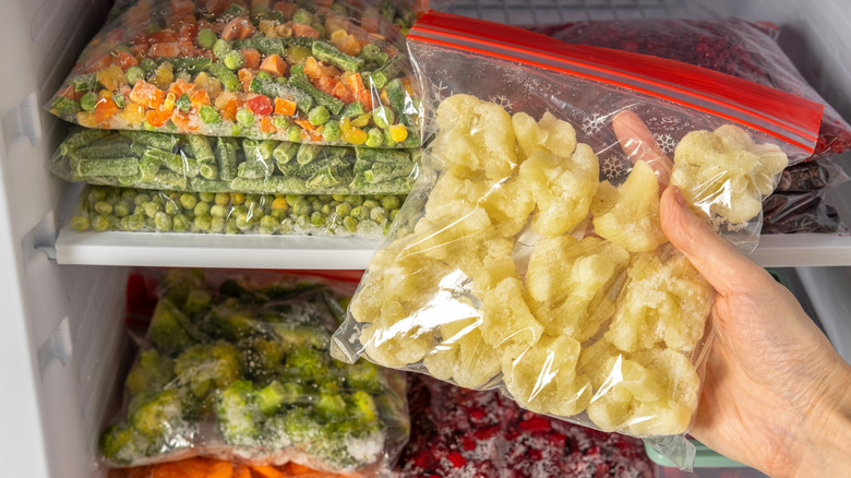 Close up of a hand taking frozen cauliflower out of a freezer full of frozen veggies.