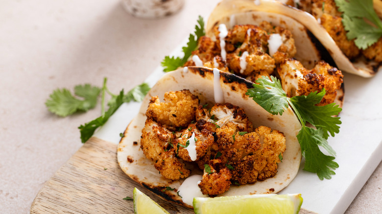 Three cauliflower tacos lined up on board with sprigs of herbs.