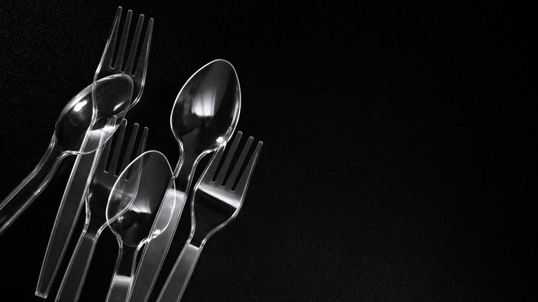 plastic forks and spoons against a black background