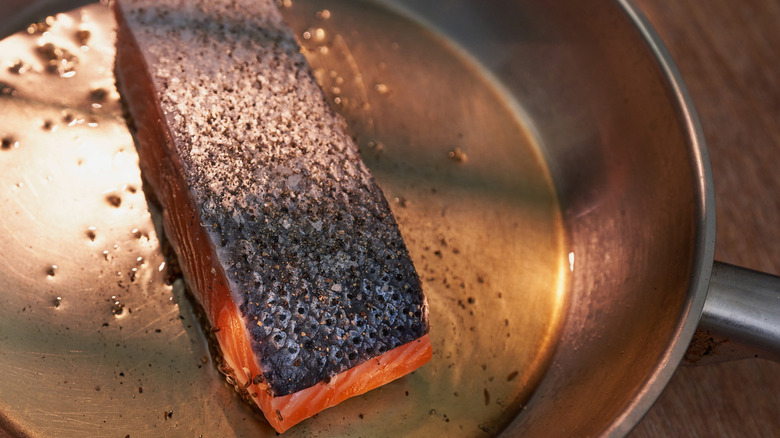 Salmon being cooked in a pan with its skin on