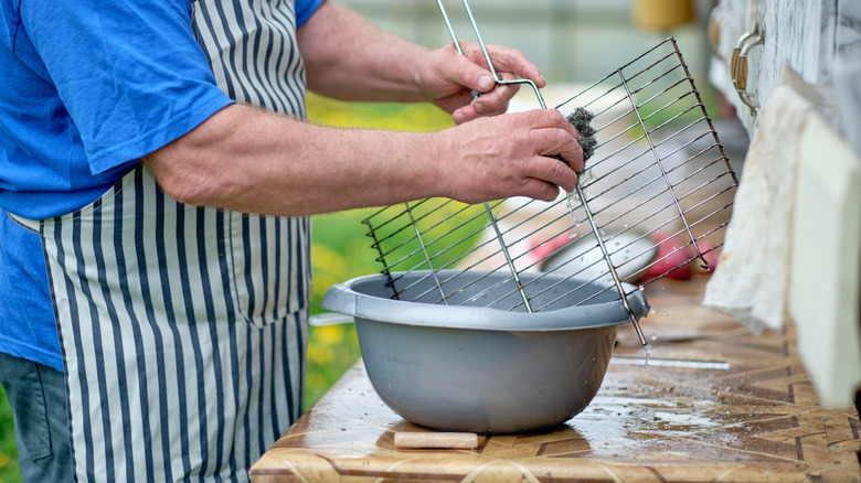 A man washing grill grates with a soft sponge