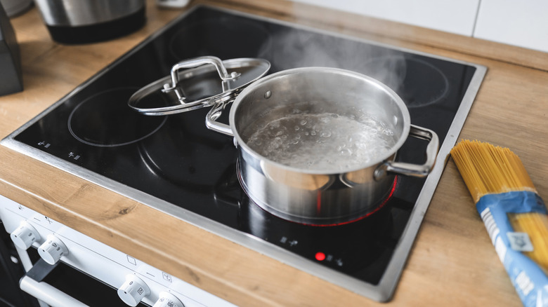 Pot of water boiling on an induction stovetop with package of dry pasta next to it