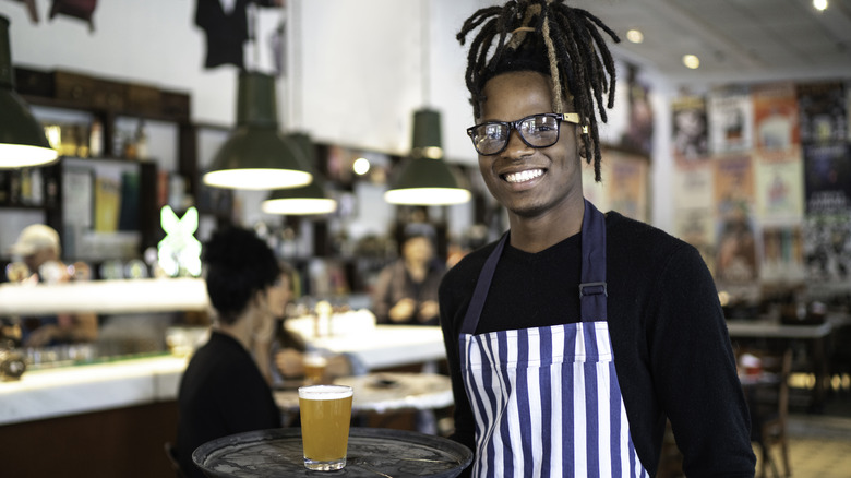 Serving carrying beer on tray while smiling