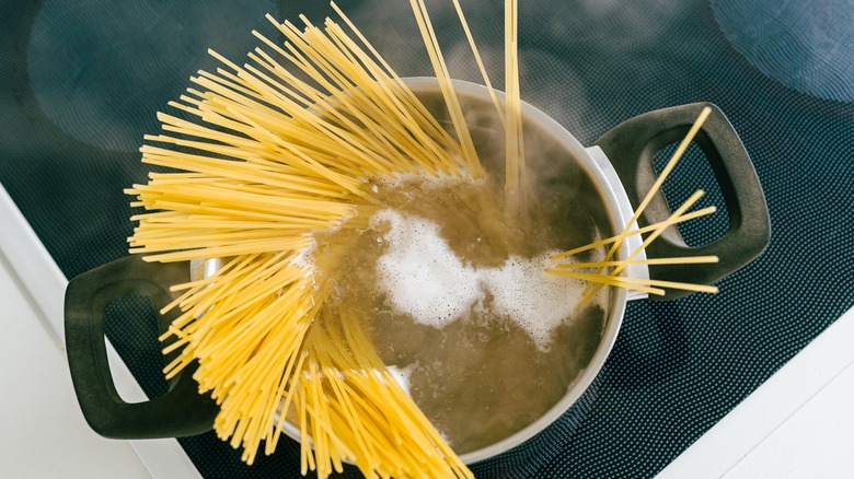 Uncooked spaghetti held above a steaming stock pot of water