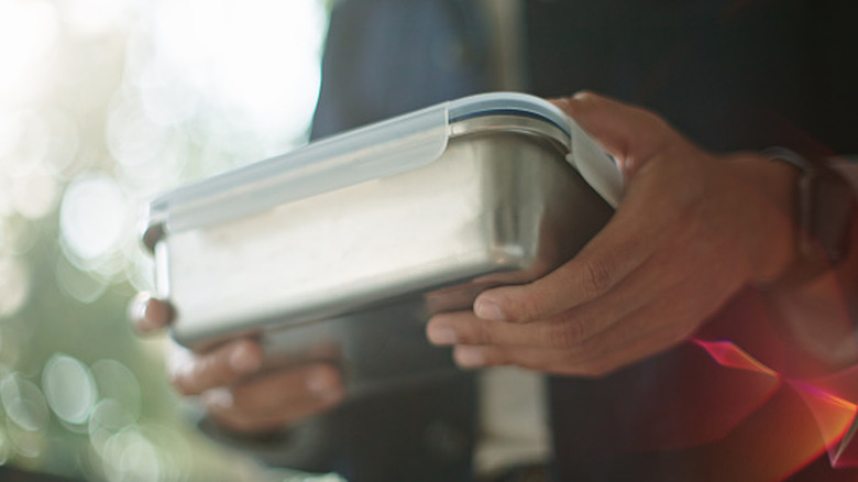 A person holding a stainless steel food container