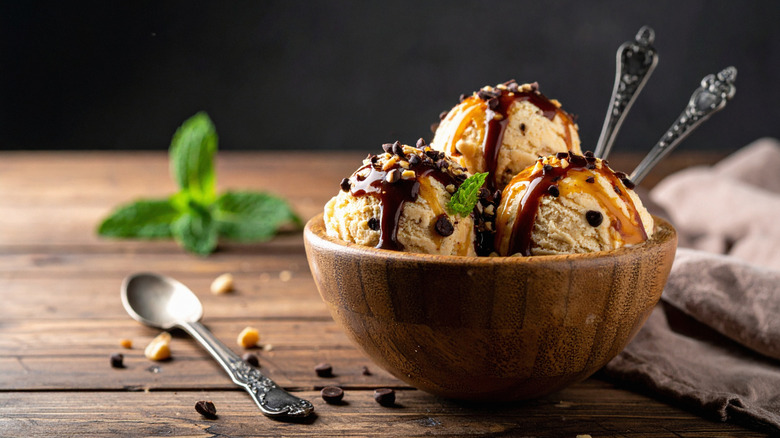 Three scoops of ice cream in bowl with chocolate sauce, chopped nuts, and mint