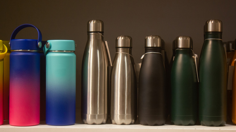 A variety of reusable water bottles ranging in color from pink-and-purple to silver to dark green on a shelf