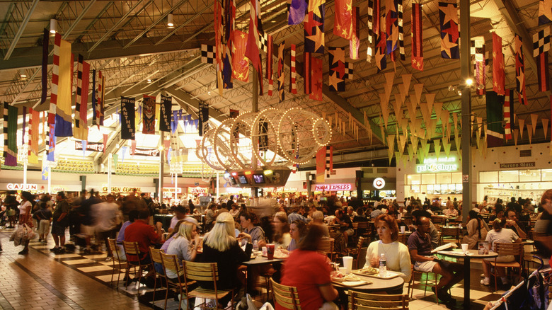 An illuminated mall food court with lots of people at tables