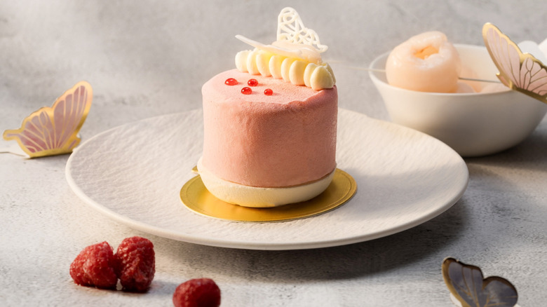 A lychee raspberry mousse artfully placed on a golden circle on a white plate