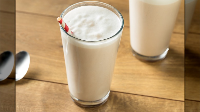 A glass of vanilla egg cream with a red and white striped straw