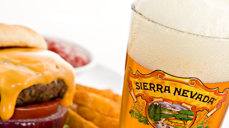 Sierra Nevada Brewing Co. logo on pint glass filled with golden beer, with a cheeseburger and fries next to it