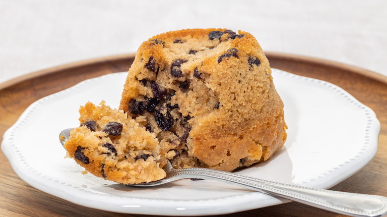 Spotted dick pudding, with a spoonful taken out of it, showing the raisins inside