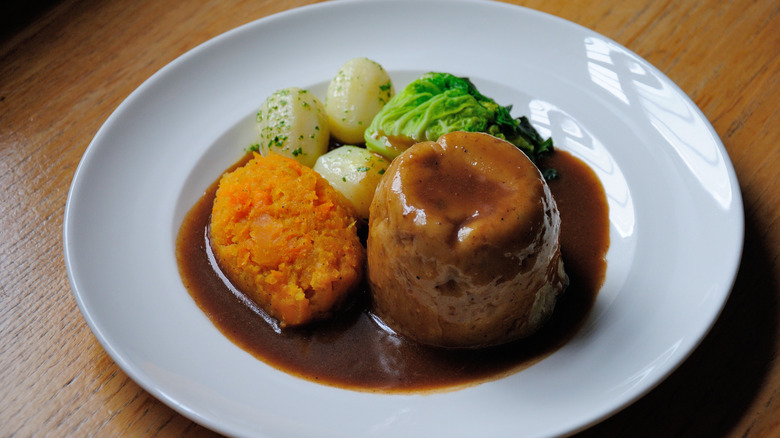 Steak and kidney pudding, served with potatoes, swede, cabbage
