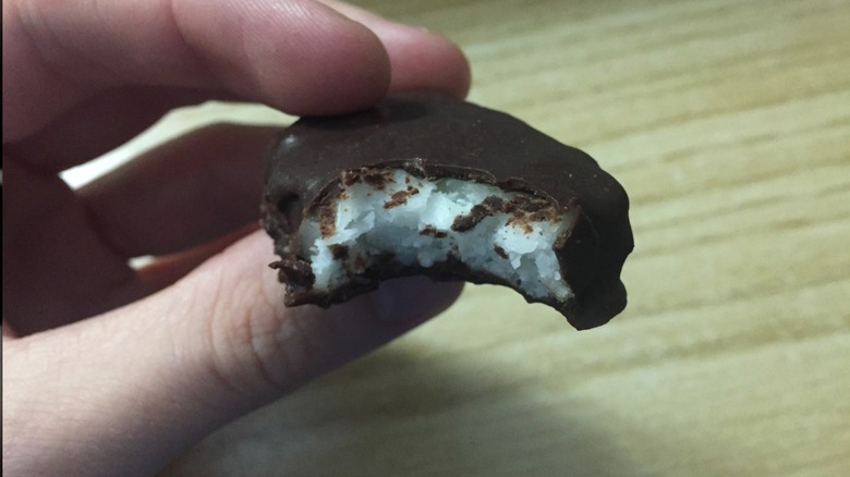 A hand holds a Needham candy with a bite taken out of it to show the filling