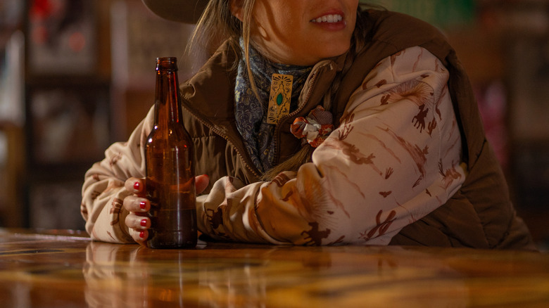 A woman in a cowboy hat drinking a beer at a bar