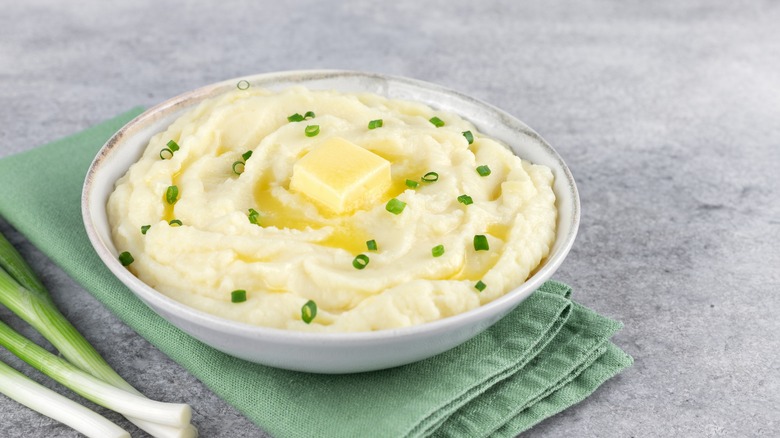 A bowl of mashed potatoes with melting butter and finely chopped green onions