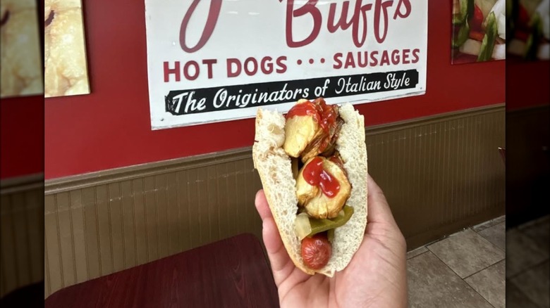 A hand holds an Italian hot dog in front of a Jimmy Buff's sign