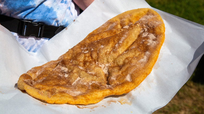 An elephant ear pastry held up on a layer of paper