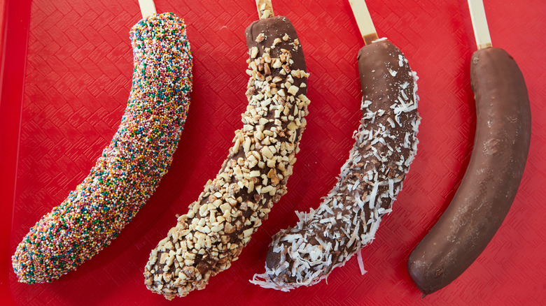 Line-up of chocolate-covered frozen bananas rolled in different toppings and posed on a red tray