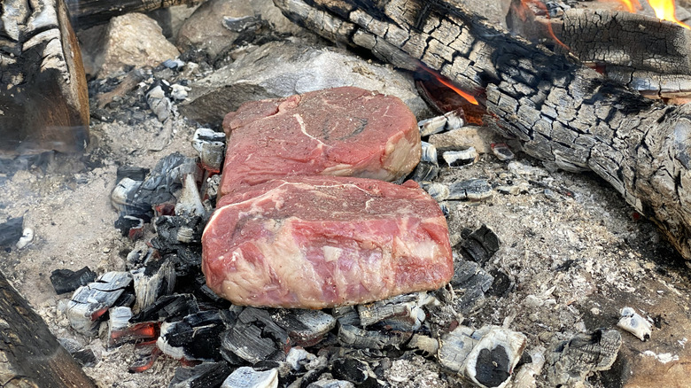 Caveman steak being cooked on coals outdoors
