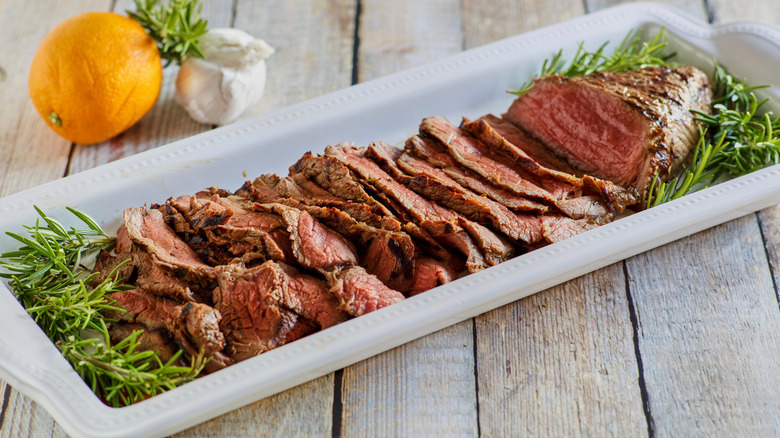 London broil with garnish on a white plate against a wooden background