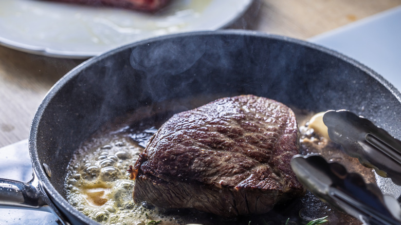 Close up of a steak being fried in a black pan