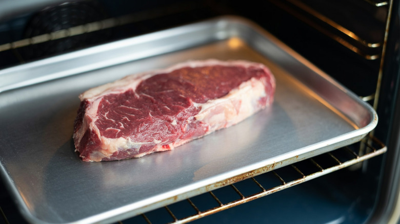 Beef steak on a metal sheet tray inside of an oven