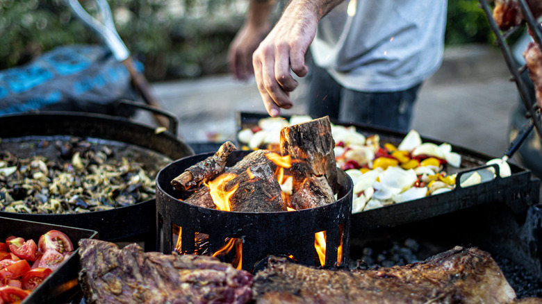 meats andc vegetables being cooked in a wood-fired grill set up