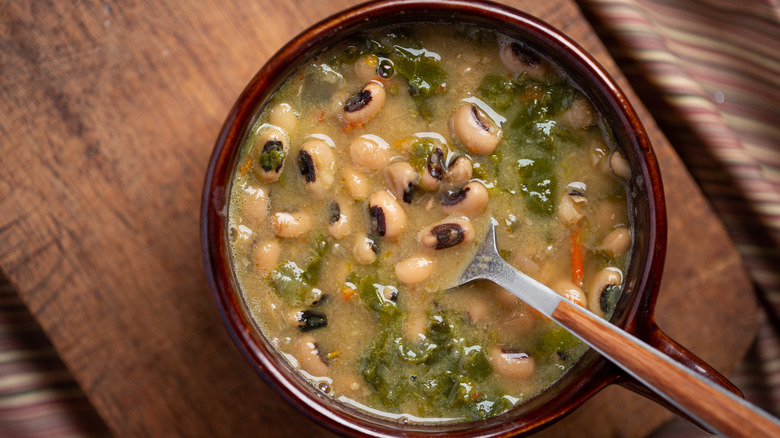 A bowl of beans and greens on a wooden cutting board