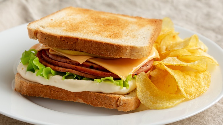 A white plate with a fried bologna sandwich and chips