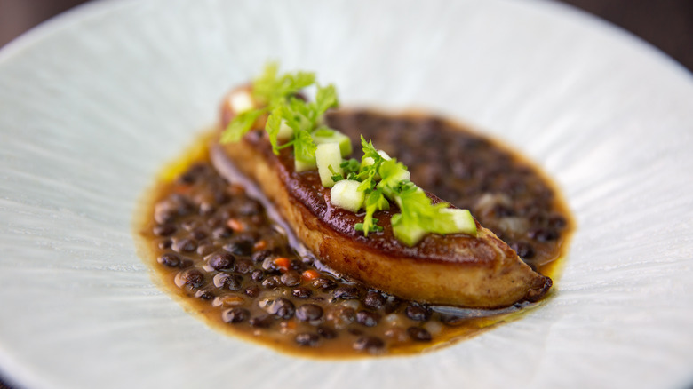 A dish of faoi gras swimming in black beans and topped with a garnish