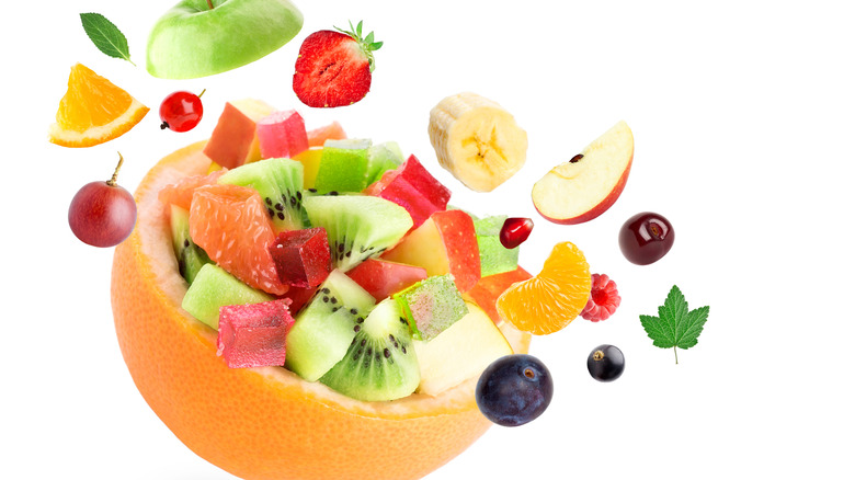 Various piece of fruit inside of and surrounding a hollowed out grapefruit