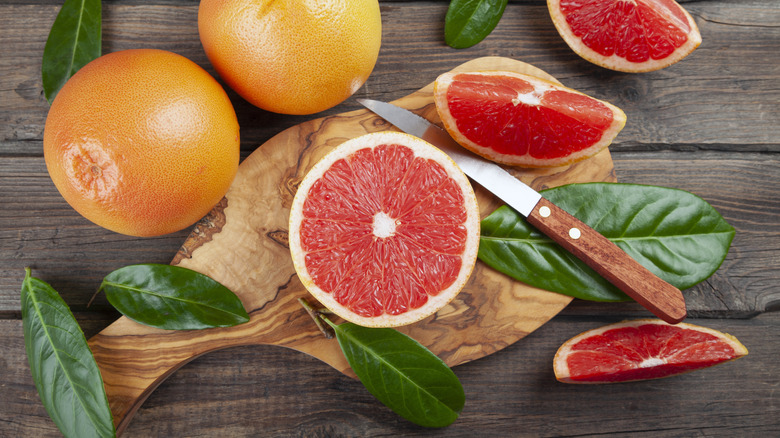 A sliced grapefruit on a cutting board next to several whole grapefruits