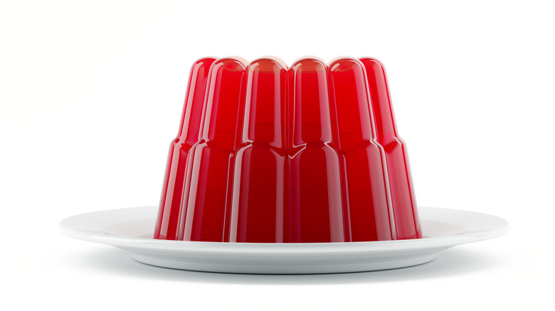 A red mold of jello on a white plate against a white background