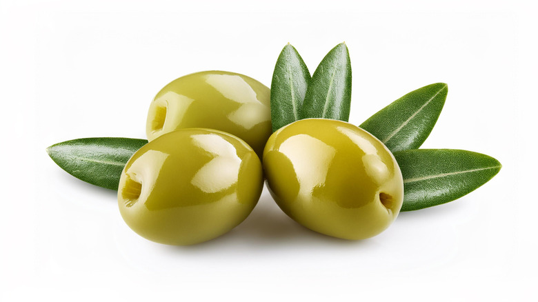 Three green olives with leaves against a white background