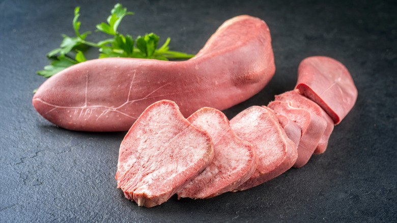 A cut up piece of cooked tongue next to an uncut piece next to a leafy garnish
