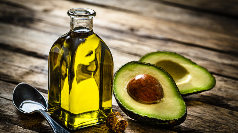 Avocado oil in glass jar with spoon and halved fresh avocadoes