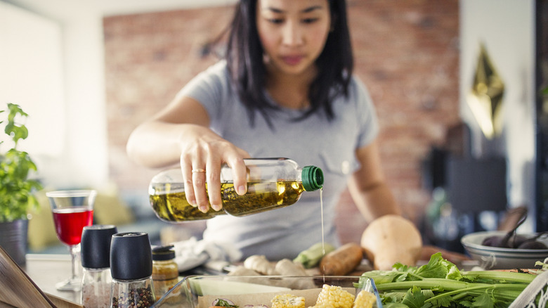 Person in kitchen pouring olive oil on vegetables.