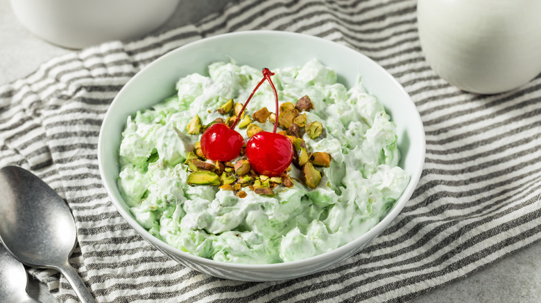 White bowl of Watergate salad with pistachios and maraschino cherries on top