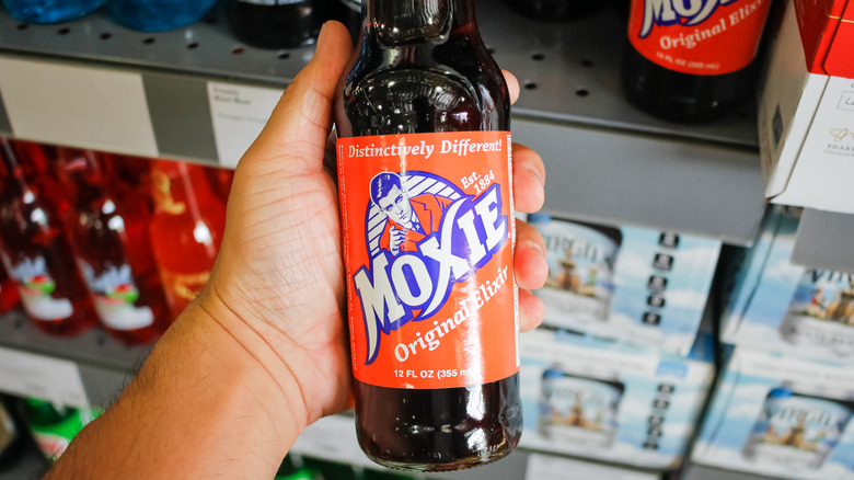 A person holds a bottle of Moxie