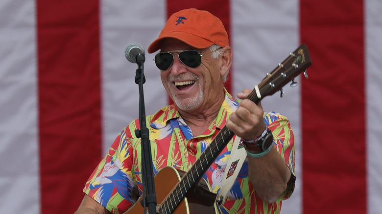 Jimmy buffett performing on stage with a guitar in front of an american flag backdrop