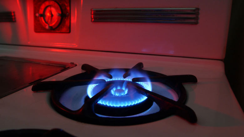Blue flame rising from a gas burner on a vintage white stove, lit with red lighting