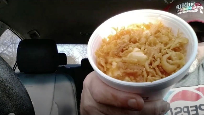 Man holding up a cup of mac and cheese with crumblies from Long John Silver's.
