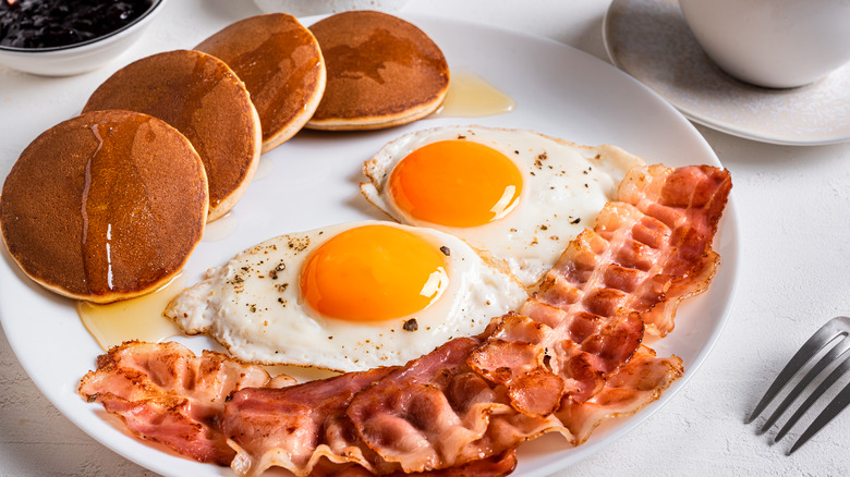A cooked breakfast, with pancakes, eggs, and bacon