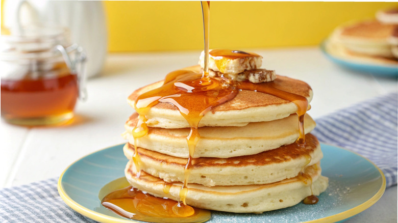 A stack of pancakes, with syrup being poured onto it