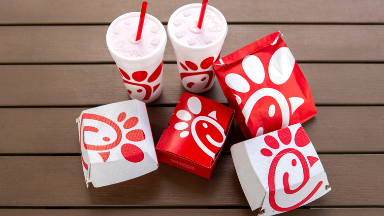 An assortment of Chick-fil-A packages and cups on a wooden surface.